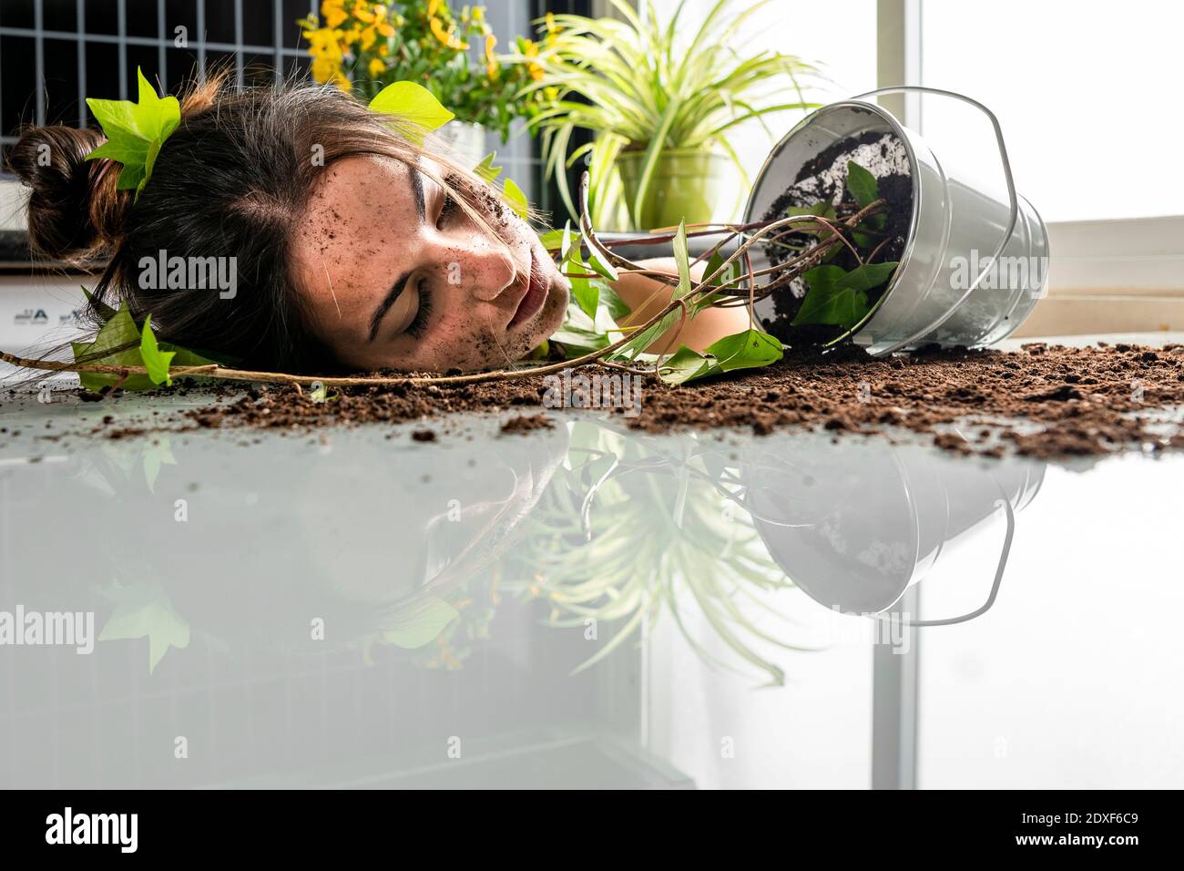 Jeune femme avec du sol sur le visage appuyé par la plante en pot sur la table Banque D'Images