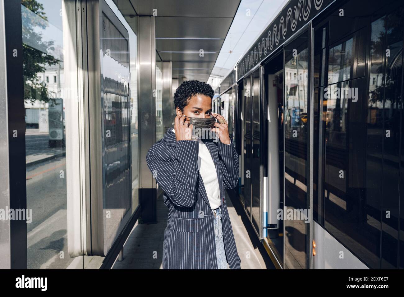 Jeune femme d'affaires portant un masque à l'arrivée du bus pendant jour ensoleillé Banque D'Images