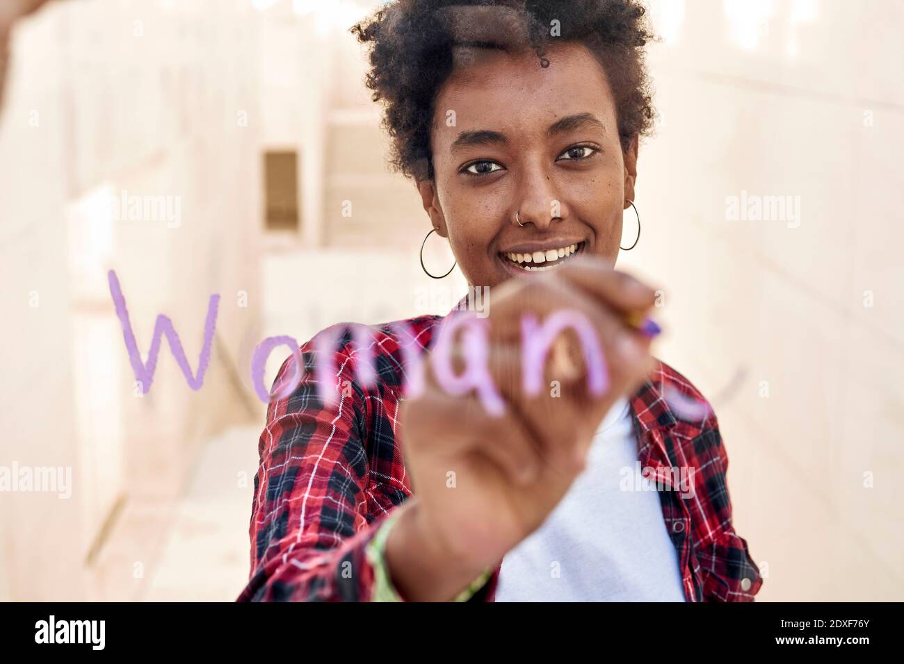 Souriante jeune femme hipster écrivant FEMME tout en célébrant la Journée des femmes Banque D'Images