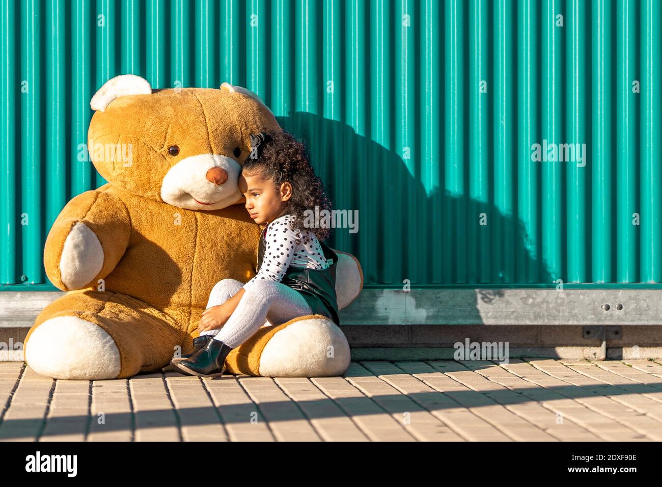 Une fille embrasse tout en étant assise avec un ours en peluche contre un mur vert Banque D'Images