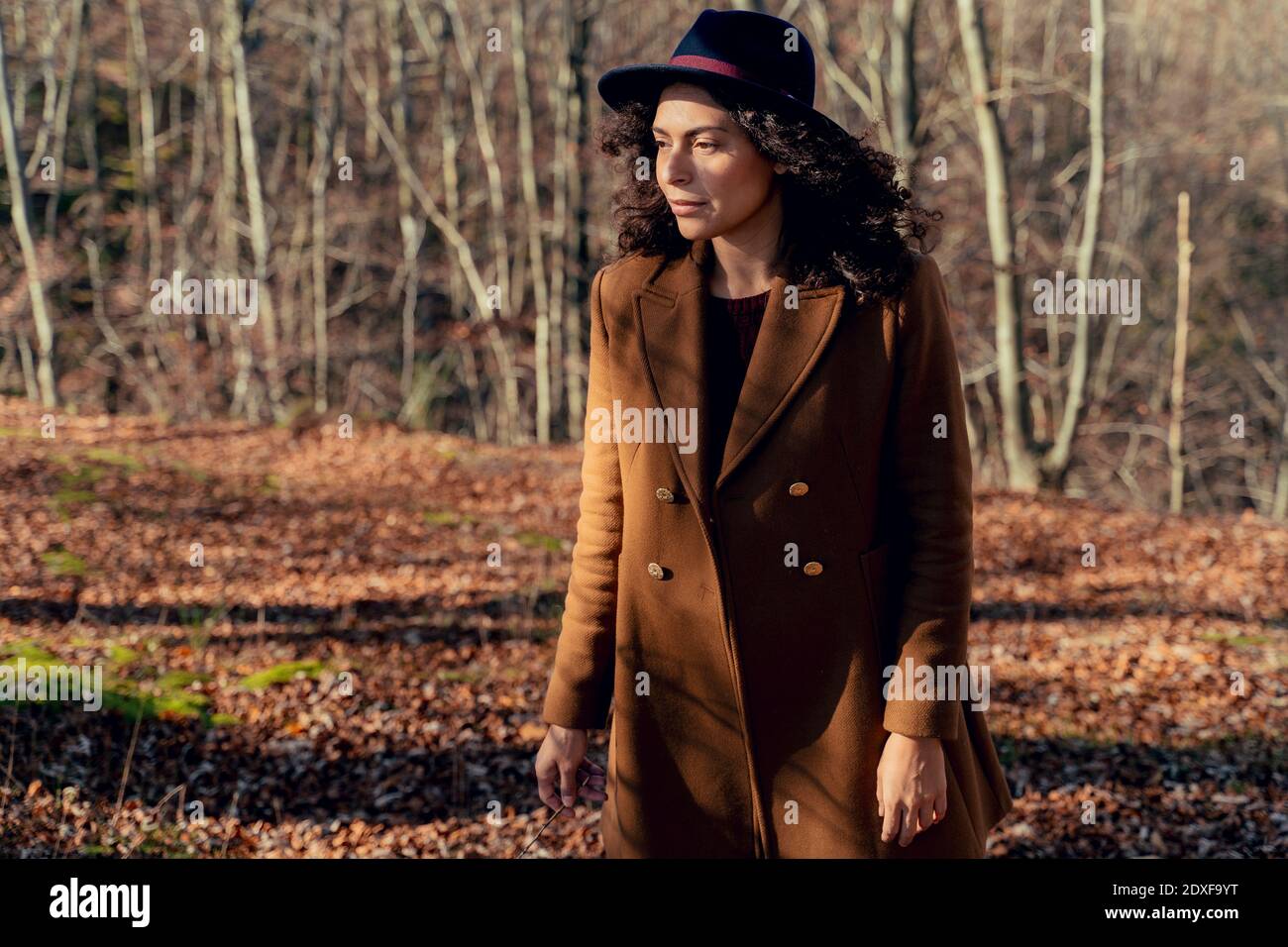 Femme portant une veste et un chapeau en regardant loin tout en restant debout forêt Banque D'Images