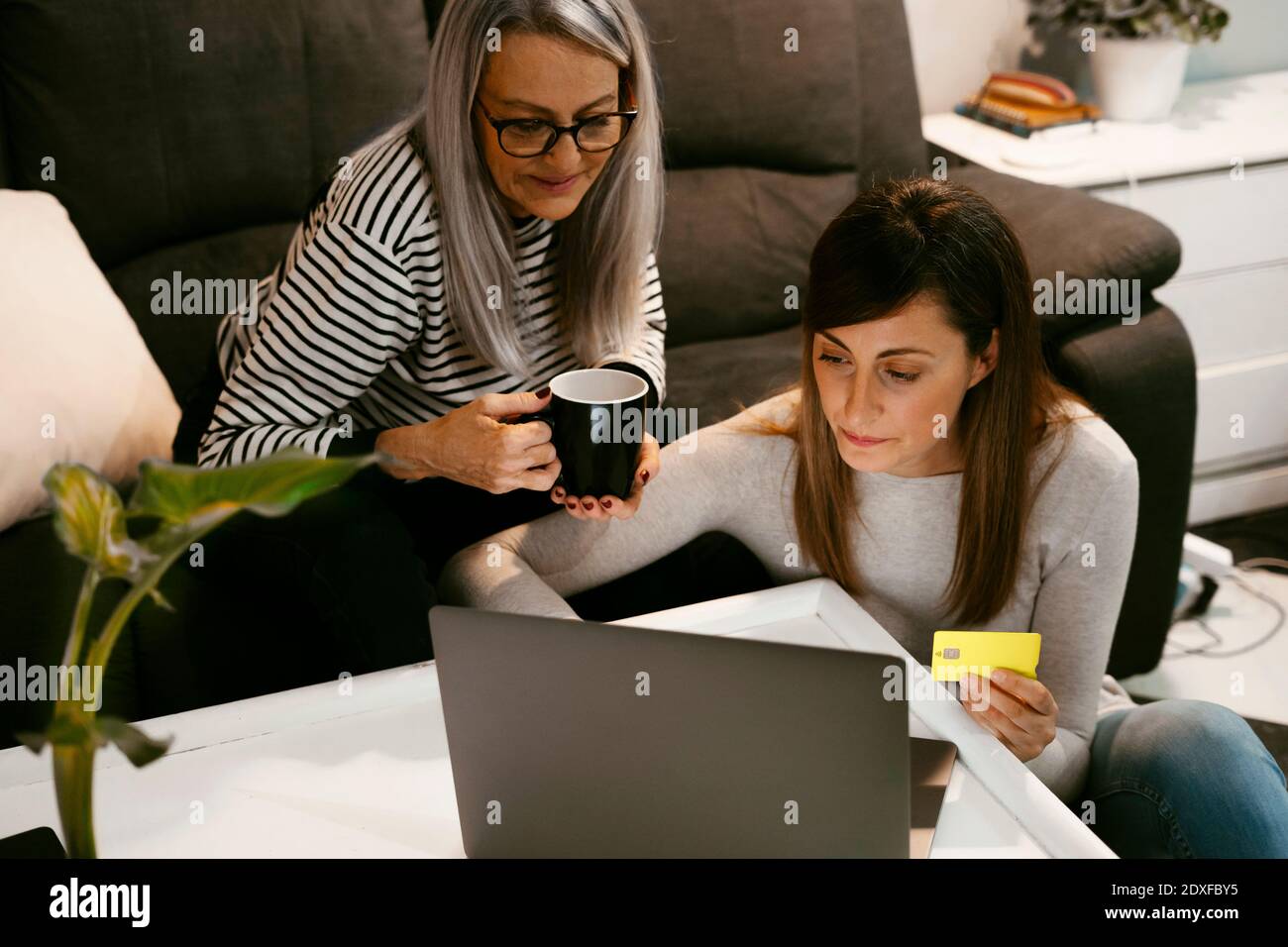 Fille avec carte de crédit qui effectue le paiement en ligne tout en étant assis mère à la maison Banque D'Images