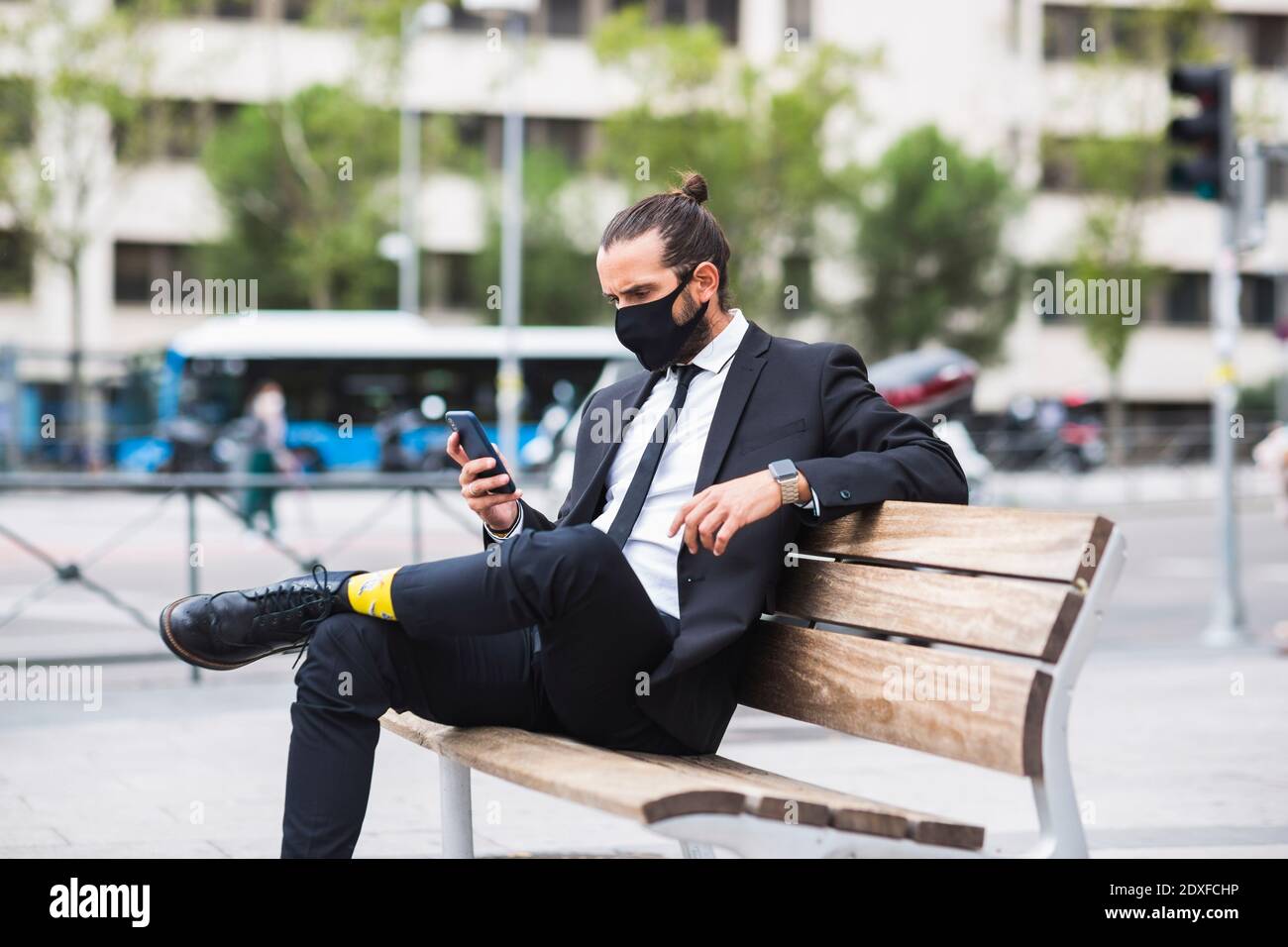 Homme d'affaires portant un masque facial de protection assis sur un banc avec élégant téléphone à portée de main Banque D'Images