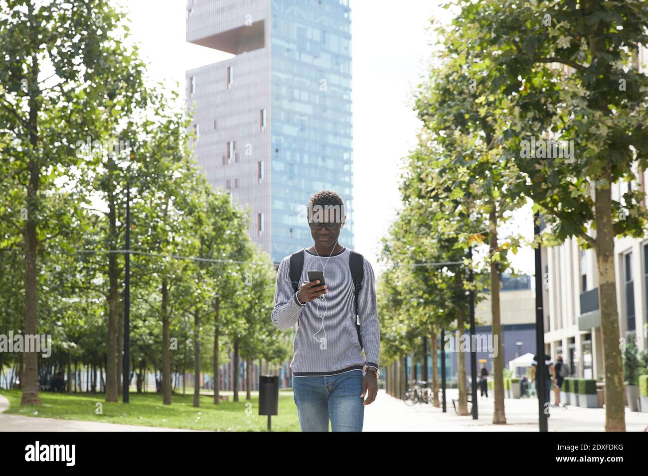 Un homme professionnel écoute de la musique avec un casque intra-auriculaire tout en marchant sentier de la ville Banque D'Images