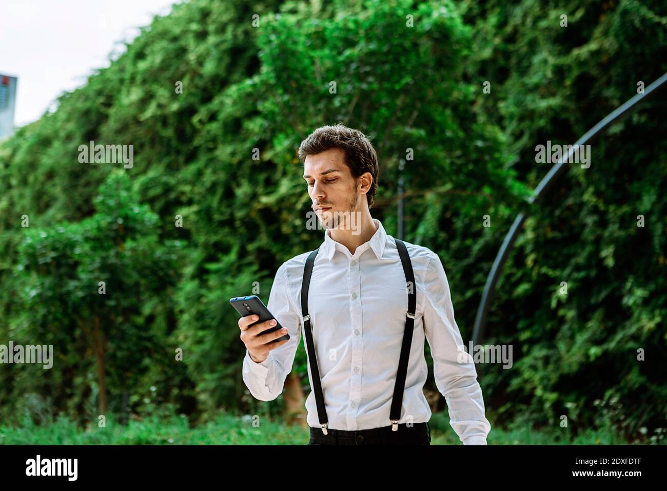 Homme d'affaires portant une chemise blanche et des bretelles noires à la  recherche d'une élégante téléphone à l'extérieur Photo Stock - Alamy