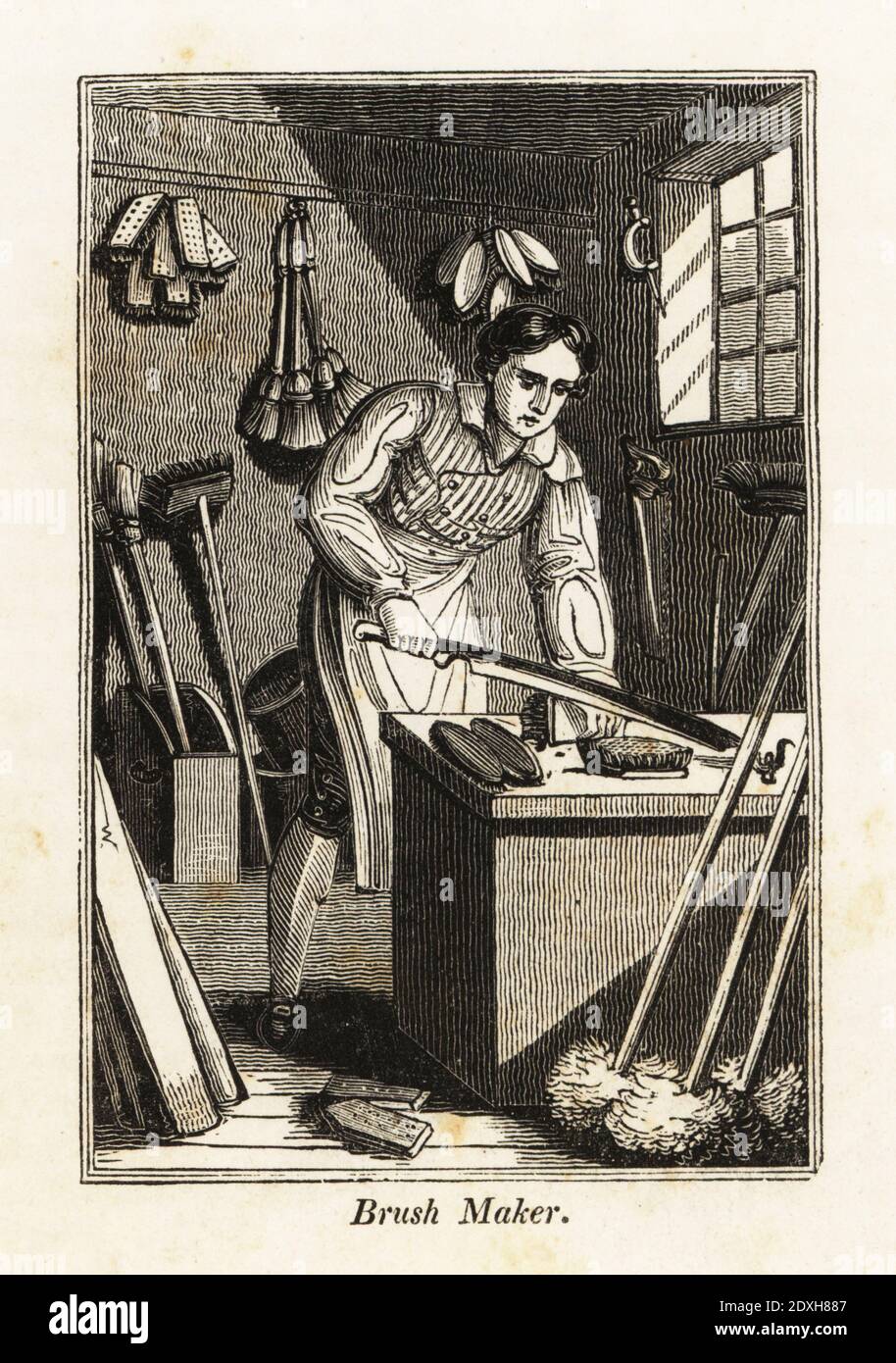 Brushmaker en tablier taille d'une tête de couveuse dans un atelier. Balais, brosses, balais et autres articles pendent des murs. Gravure en blocs de bois du Livre des métiers d'anglais, ou Bibliothèque des arts utiles, F.C.& J. Rivington, Londres, 1821. Banque D'Images