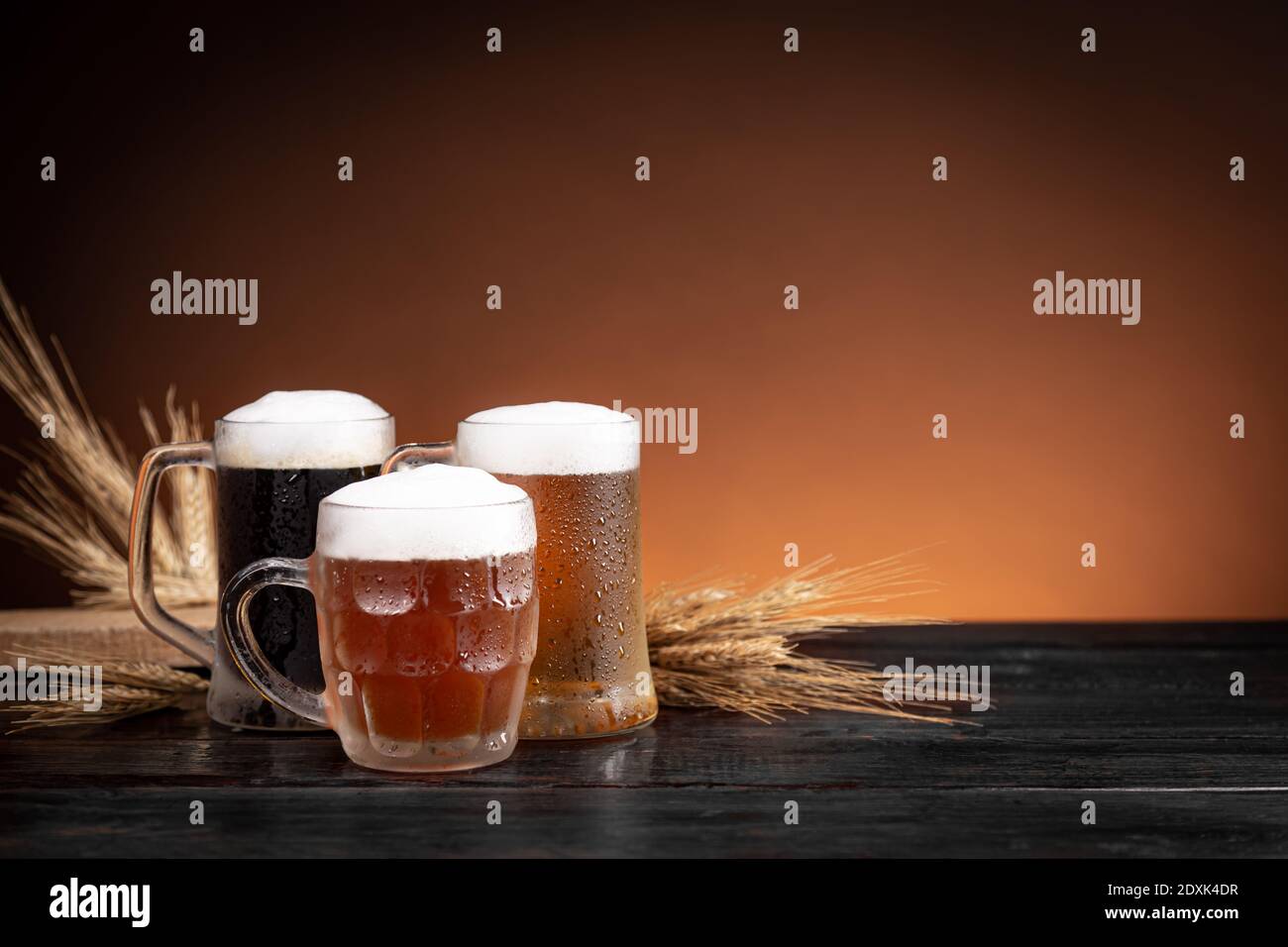 Trois types de bière froide en cruches et épis de blé à base de bois. Banque D'Images