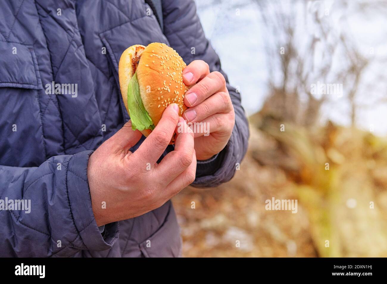 Beefburger avec un pain blanc aux graines de sésame. Pause déjeuner pendant le voyage. Restauration rapide pour le déjeuner, plats à emporter. La main contient un délicieux hamburger frais. Banque D'Images