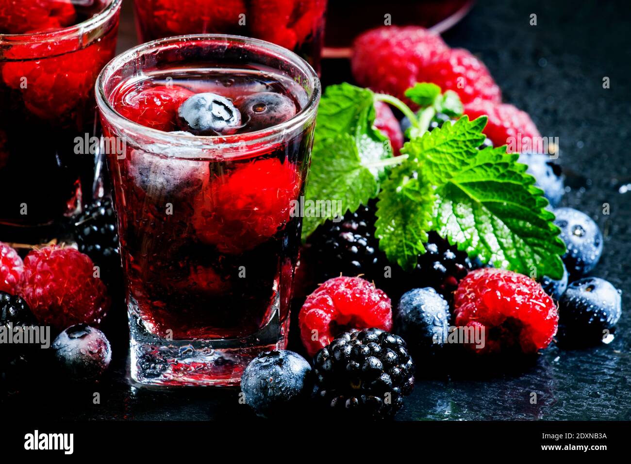 Thé froid aux baies d'été avec framboises, bleuets, mûres et menthe dans des verres embués sur un fond sombre, foyer sélectif Banque D'Images