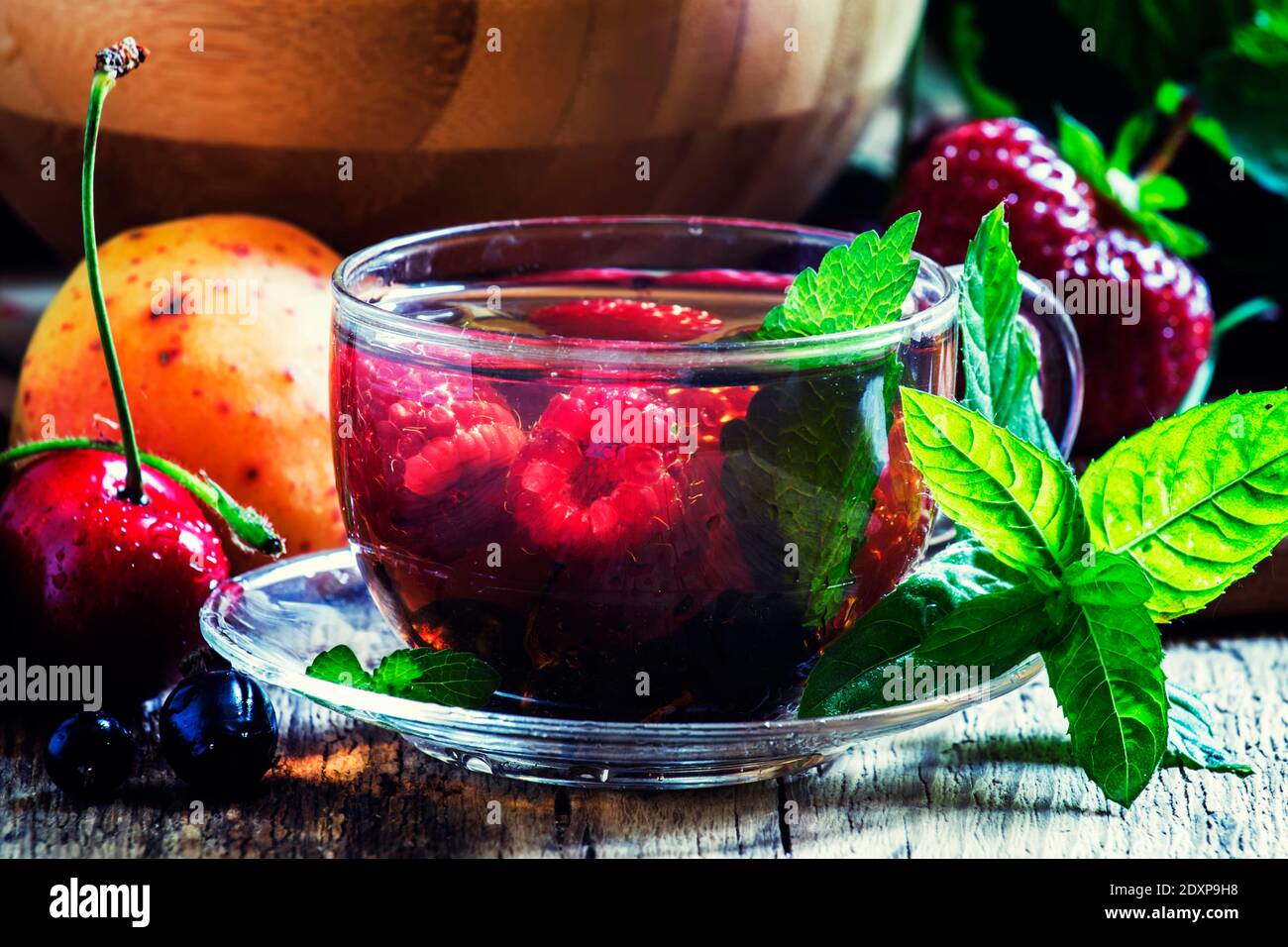 Thé aux fruits d'été avec menthe dans une tasse de verre, fruits frais et baies, fond en bois foncé, foyer sélectif Banque D'Images