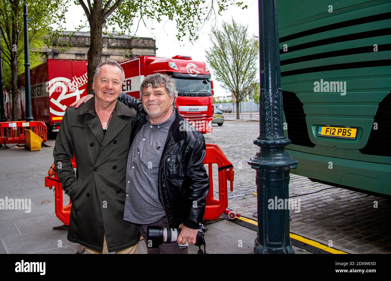 Le groupe de rock simple Minds des années 80 vient d'arriver à Dundee, en Écosse, pour le début de leur tournée britannique du 17 mai 2017. Jim Kerr debout [à gauche] du photographe local devant l'entrée de la scène arrière du Caird Hall avec une presse associée et un photographe Dundee local avant leur concert en direct acoustique Banque D'Images