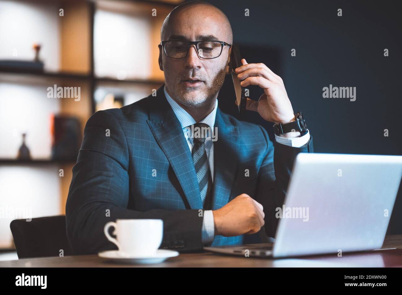 En répondant à un appel téléphonique, un homme d'affaires a pris une pause au travail et regarde une tasse de café près d'un ordinateur portable. Beau homme audacieux travaillant sur un ordinateur portable Banque D'Images