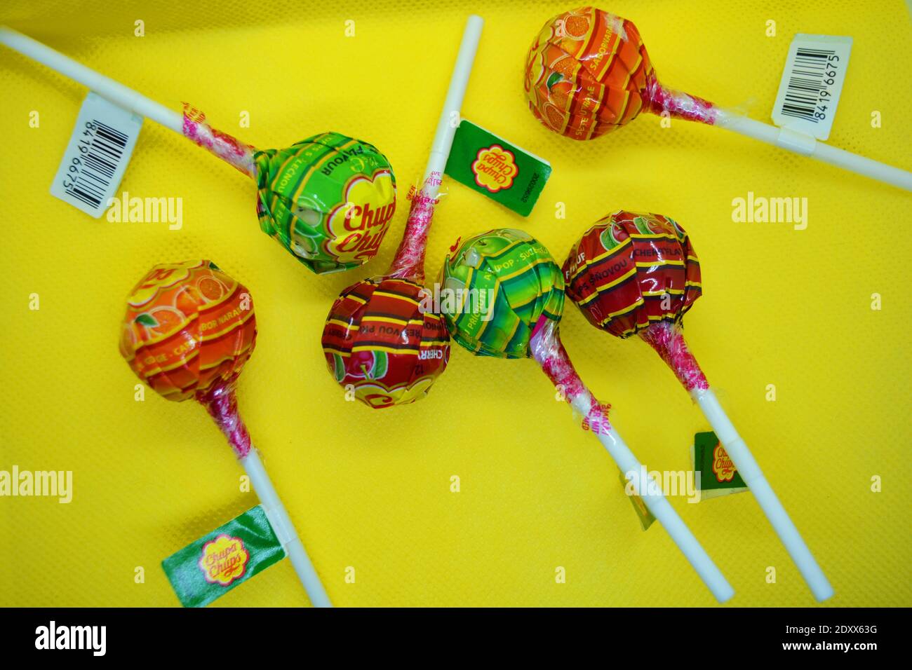 Une poignée de bonbons populaires, colorés et lumineux, lidintsi ronde avec un bâton en plastique blanc sur fond de tissu jaune. Banque D'Images