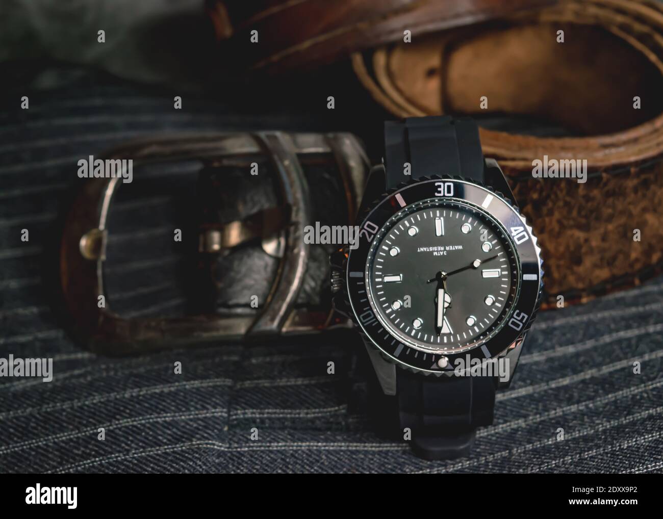 Gros plan d'une montre en chrome noir, d'une boucle de ceinture en cuir et d'une partie d'un bracelet en cuir sur un tissu gris Banque D'Images