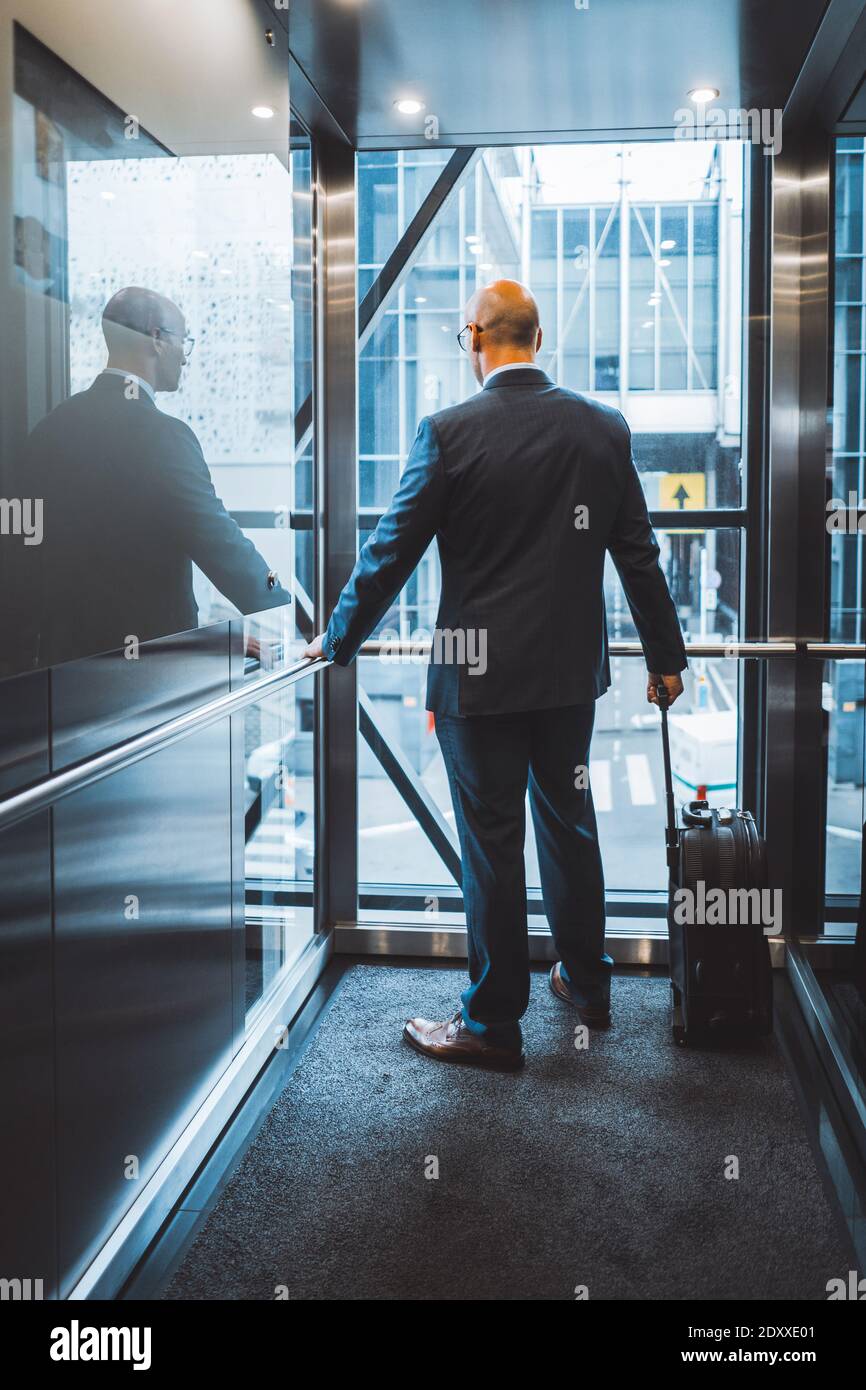 Un homme d'affaires est arrivé à l'hôtel pour un voyage d'affaires la colonie se lève dans l'ascenseur debout avec son dos à la caméra tenant une valise près du Banque D'Images