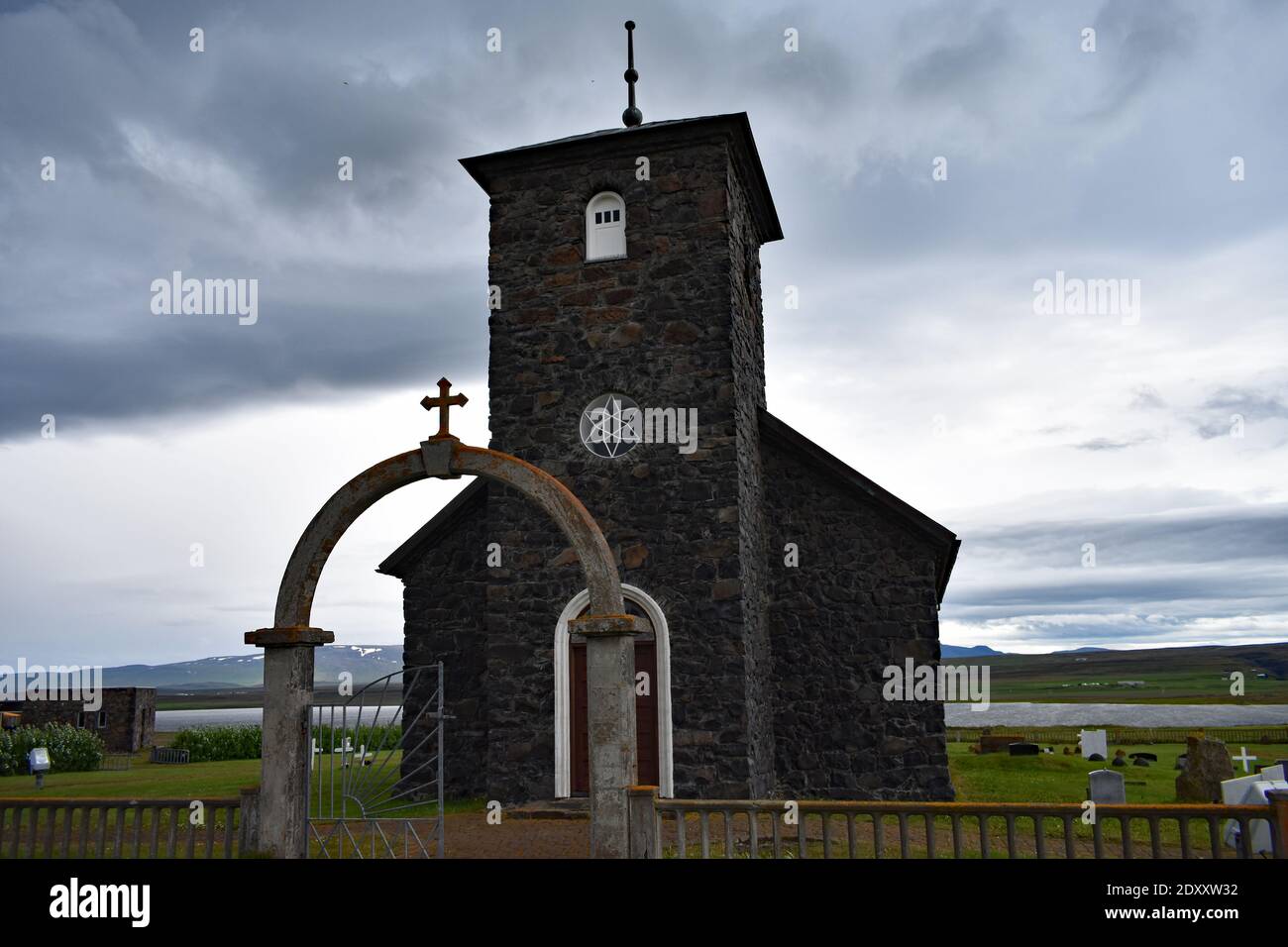 Église de Thingeyrar, ÉGLISE en pierre du XIXe siècle dans le nord de l'Islande. Une porte voûtée avec une croix mène au petit bâtiment noir par une journée. Banque D'Images