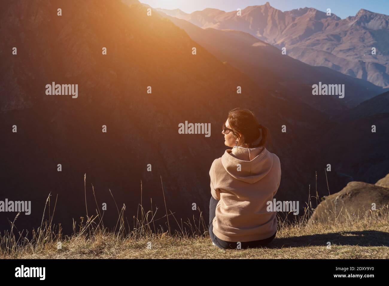 Une brunette enchantée en lunettes de soleil se trouve sur le bord de colline de l'herbe brune et regarde les paysages vallonnés sous la lumière du soleil à l'automne vue de jour Banque D'Images