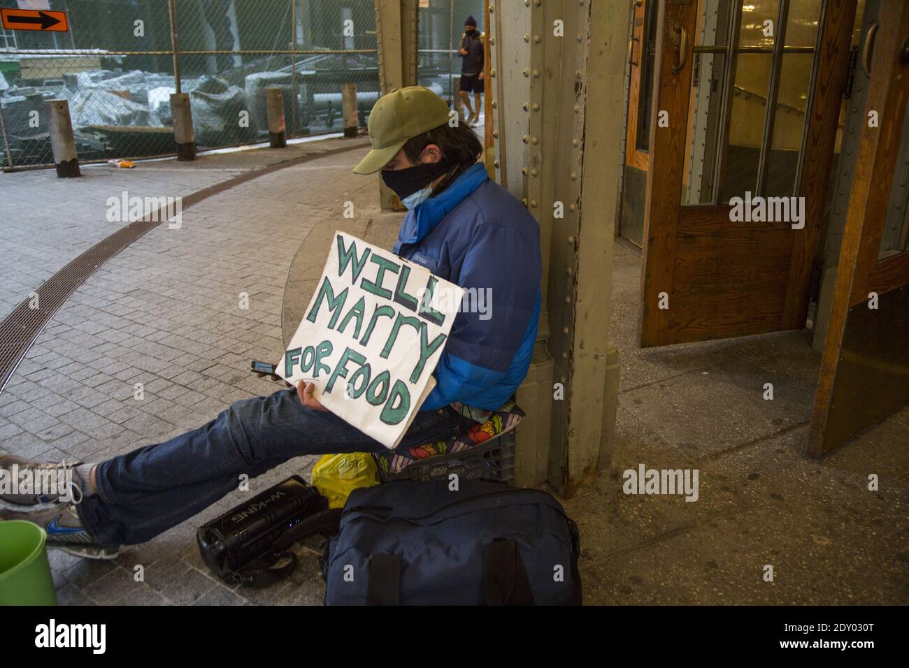 Un homme sans abri avec un sens de l'humour se trouve devant une entrée du Grand Central terminal à Manhattan, New York. Son panneau indique va se marier pour la nourriture. Banque D'Images