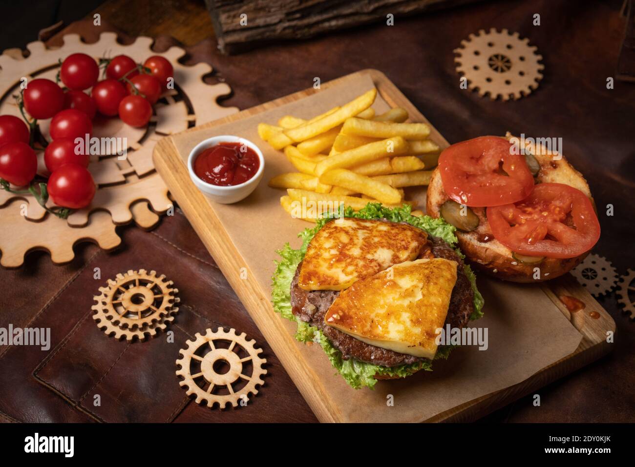Hamburger démonté ou semi-fini au fromage frit, tomate servie avec des frites sur un panneau décoratif en bois avec sauce tomate et bois Banque D'Images