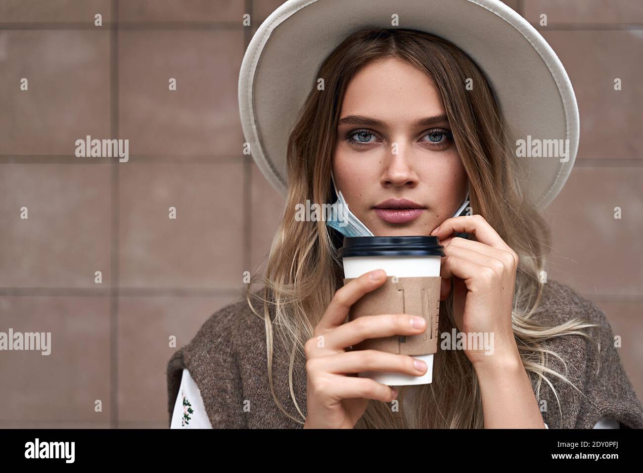 Fin du verrouillage de quarantaine. Une fille vaccinée boit du café tout en tirant sur le masque de protection Banque D'Images