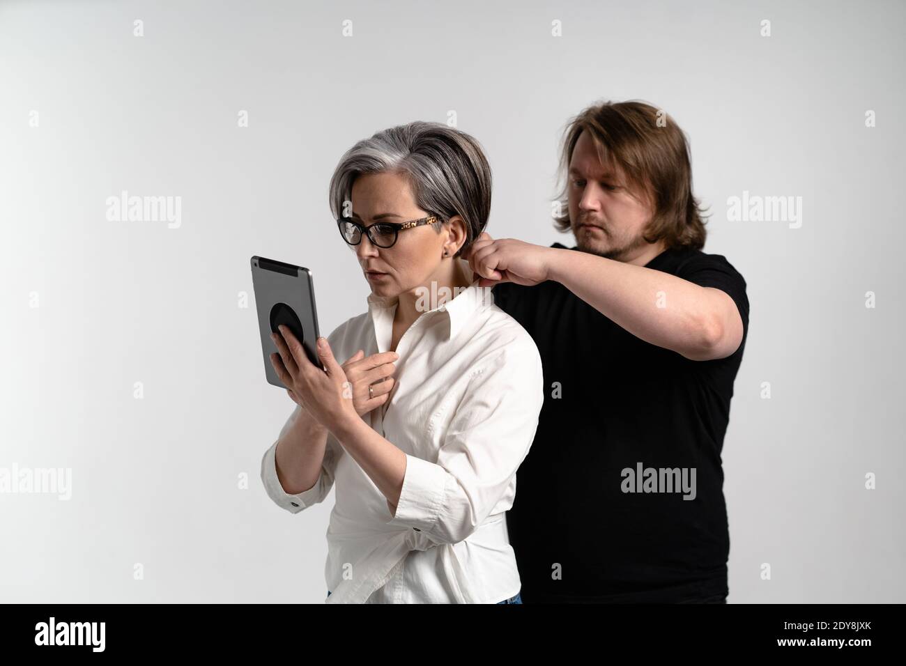 Le styliste ajuste le costume du présentateur ou du blogueur avant d'aller à la télévision, une femme adulte lit le texte à l'aide d'une tablette numérique isolée Banque D'Images