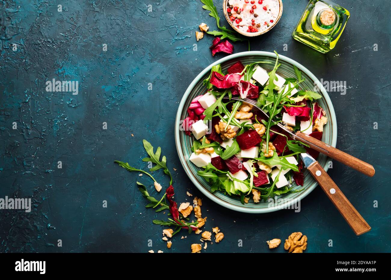 Salade de betteraves ou de betteraves à l'arugula fraîche, au radicchio, au fromage doux et aux noix sur l'assiette avec fourchette, vinaigrette et épices sur fond bleu de table de cuisine Banque D'Images