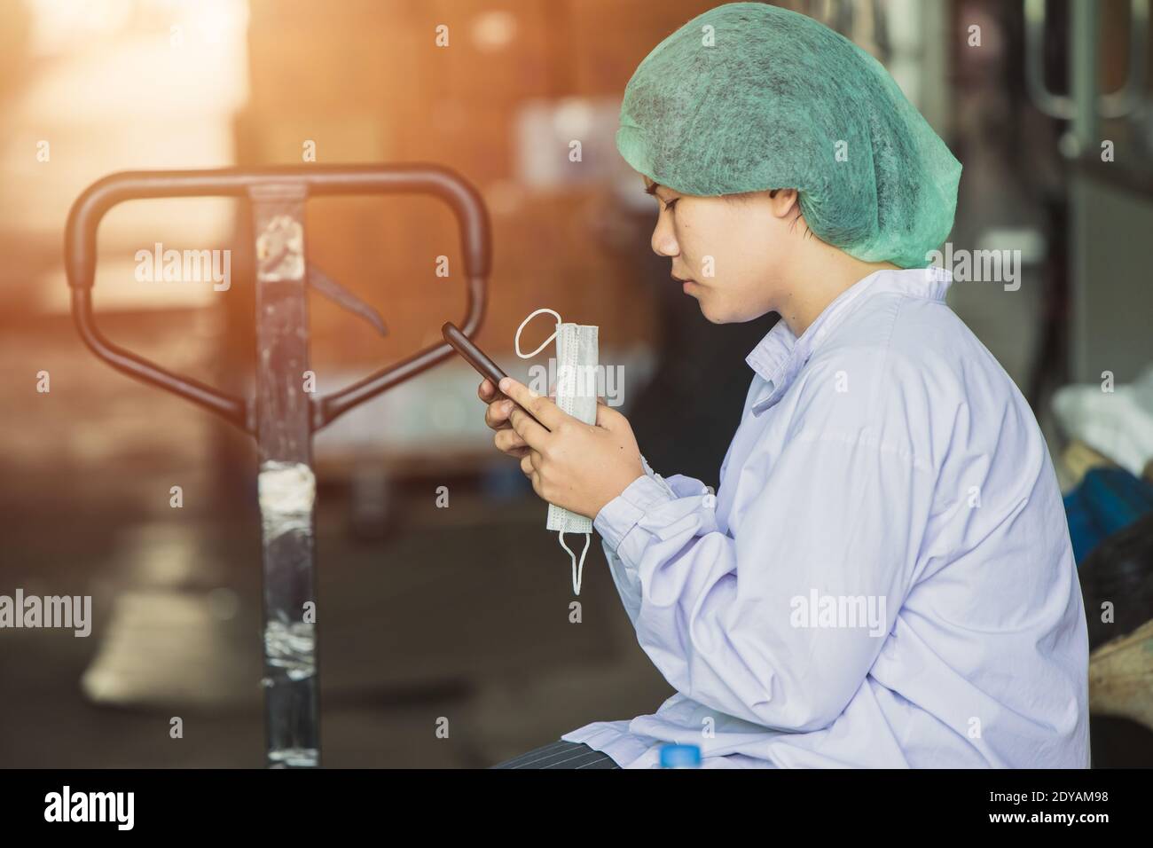 Une jeune femme birmane asiatique travaille pour se détendre, jouant au téléphone portable, attendant des quarts de travail dans une usine d'hygiène alimentaire. Banque D'Images