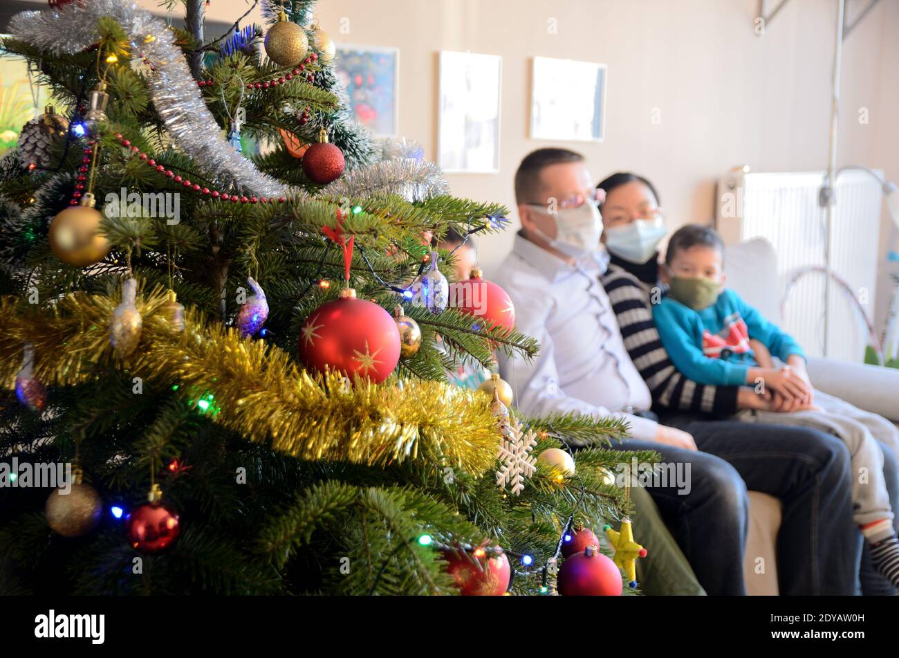 Vacances avec Covid-19, arbre de Noël en direct décoré avec la famille rougie en arrière-plan avec des masques jetables. Banque D'Images