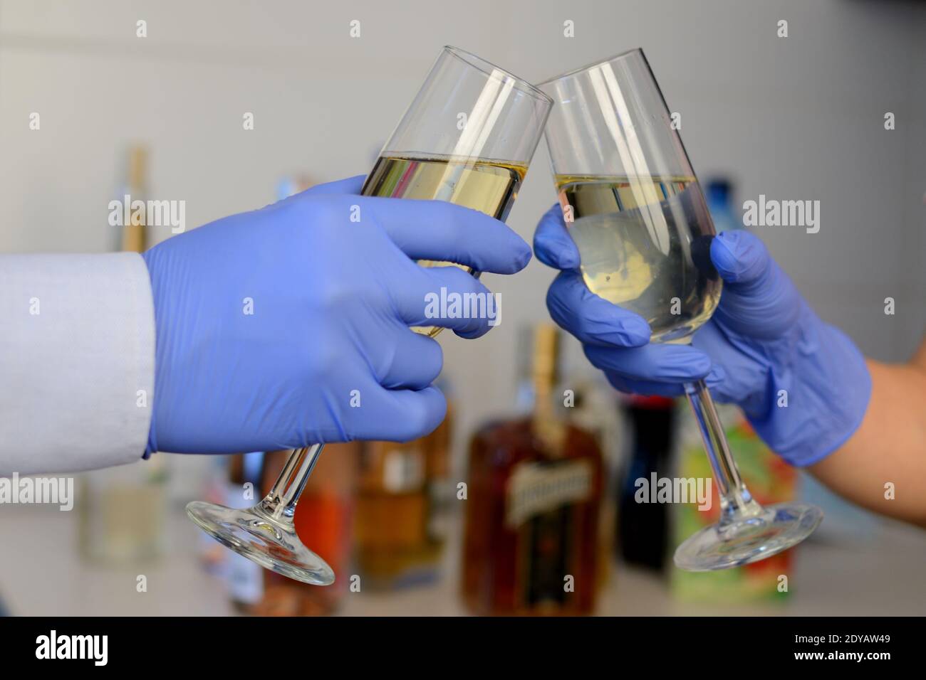 Fête du nouvel an pendant la pandémie Covid-19. Une coupe de champagne étant tenue entre les mains avec un gant bleu jetable. Banque D'Images