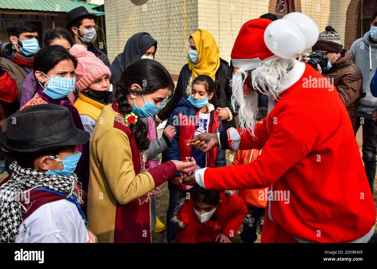 Un homme vêtu d'un costume du Père Noël distribue des bonbons parmi les enfants à l'extérieur de l'église catholique de la Sainte famille pendant Noël. Banque D'Images