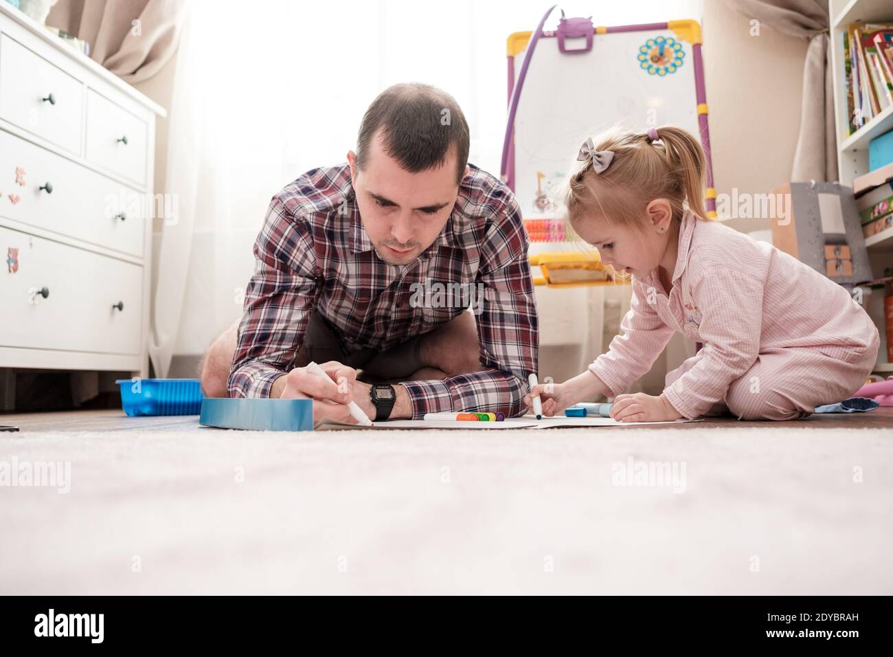 Père et fille dessiner avec des marqueurs de couleur tout en étant assis sur le sol dans la chambre. Garde et développement des enfants. Banque D'Images