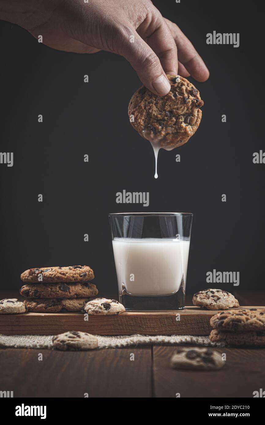 Biscuit au chocolat en trempant à la main dans un verre de lait. Sur fond en bois, fond sombre. Concept de nourriture douce. Banque D'Images