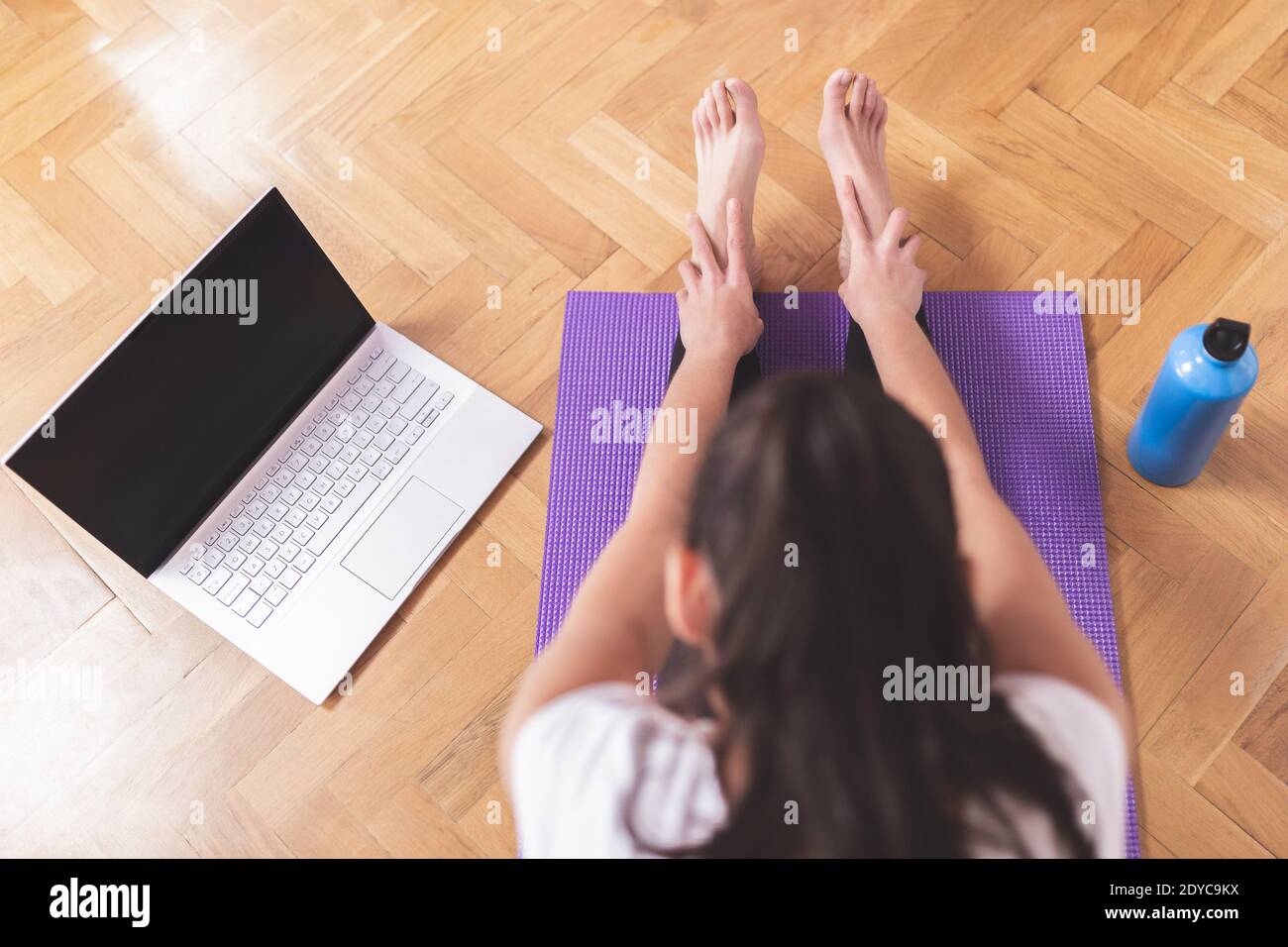 Jeune femme caucasienne heureuse, s'étirant dans le salon tout en regardant son ordinateur portable. Concept de soins de santé et de bien-être à domicile. Banque D'Images