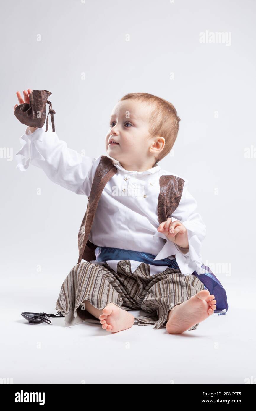 Joyeux petit garçon caucasien, habillé comme un pirate jouant avec des pièces de monnaie et des confettis sur fond blanc. Petit garçon et le concept de costumes. Banque D'Images