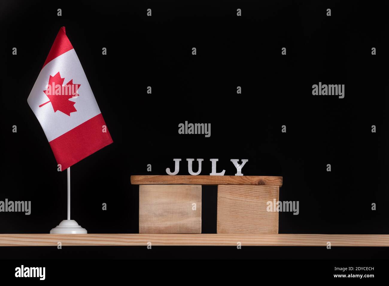 Calendrier en bois de juillet avec drapeau canadien sur fond noir. Vacances d'été au Canada. Banque D'Images