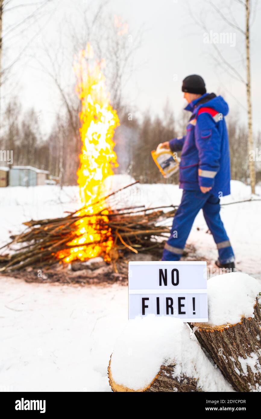 Un homme dans un uniforme bleu verse de l'essence d'une cartouche dans le feu. Ouvrir l'avertissement d'incendie. Un panneau avec le texte pas de feu. Banque D'Images