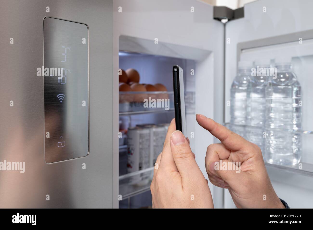 La main de l'homme qui contrôle le réfrigérateur avec son smartphone. Concept d'Internet des objets Banque D'Images