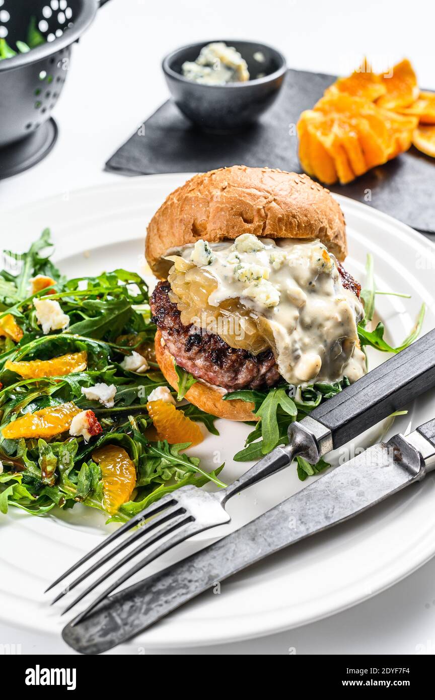 Hamburgers au fromage bleu, bœuf marbré et marmelade d'oignons, accompagnement de salade avec des arugula et des oranges. Arrière-plan blanc. Vue de dessus Banque D'Images