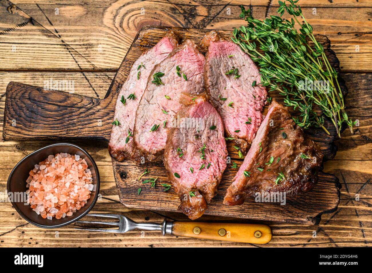 Tranches rares de rôti de boeuf sirloin à trois pointes steak bbq sur une planche à découper en bois. fond en bois. Vue de dessus Banque D'Images