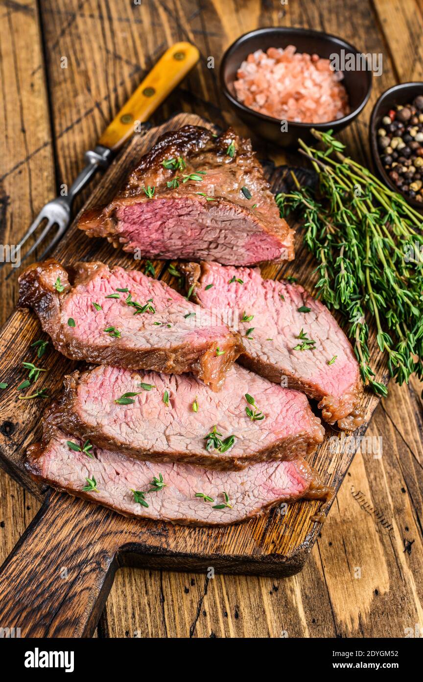 Tranches rares de rôti de boeuf sirloin à trois pointes steak bbq sur une planche à découper en bois. fond en bois. Vue de dessus Banque D'Images