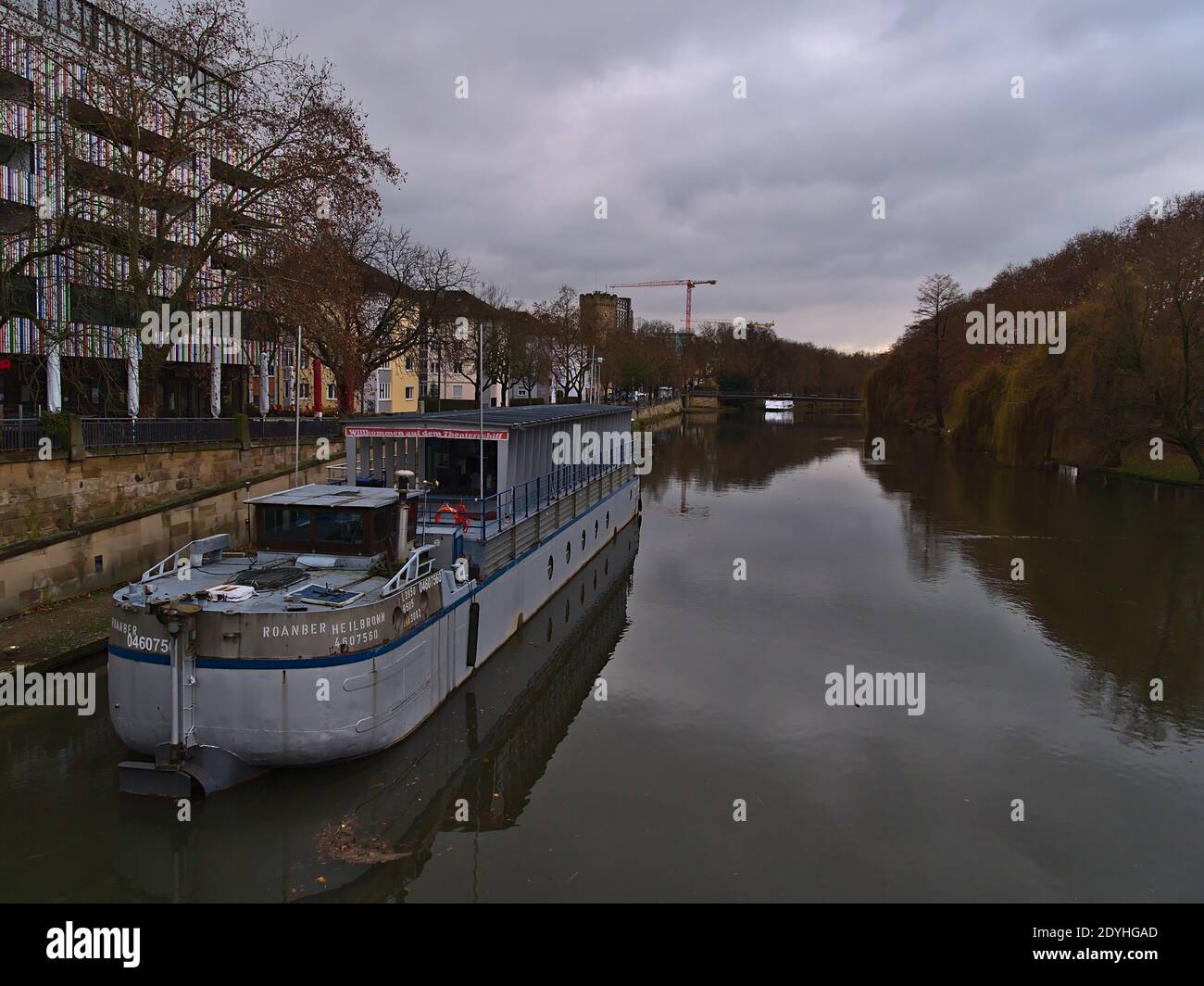 Belle vue sur la rivière Neckar dans le centre-ville avec bateau à voile, bâtiments, arbres et réflexions d'eau le jour nuageux en hiver. Banque D'Images