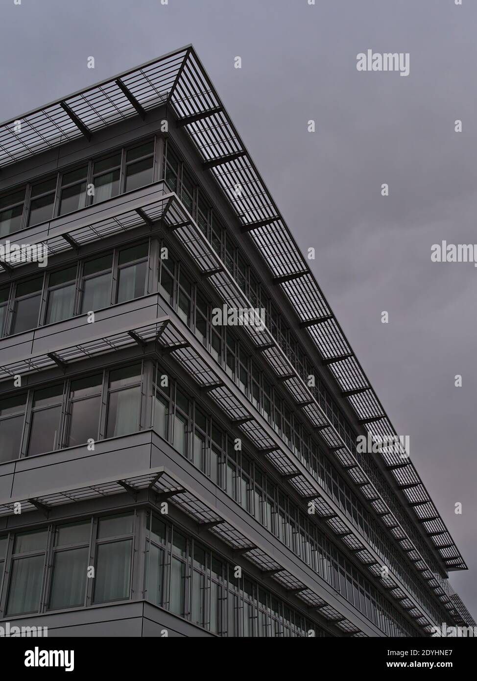 Vue à angle bas de la façade d'un immeuble de bureaux moderne avec fenêtres en verre et éléments métalliques situés dans un parc commercial par temps nuageux. Banque D'Images