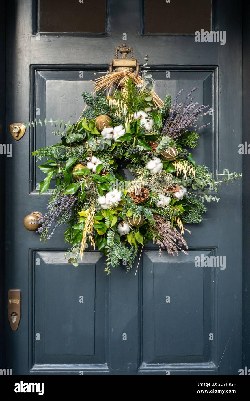 Couronne de Noël avec feuilles de lierre, baies, cônes et lavande sur une porte noire, Royaume-Uni. Décorations de saison naturelles. Banque D'Images