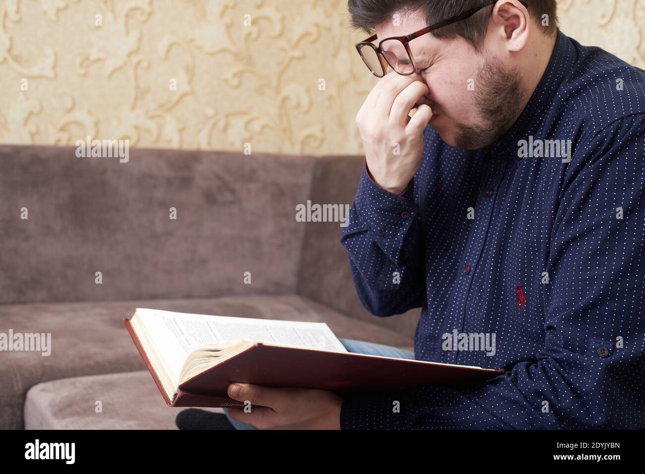 Concept, l'homme caucasien portant des lunettes a des yeux douloureux tout en lisant un livre, des copies de l'espace Banque D'Images