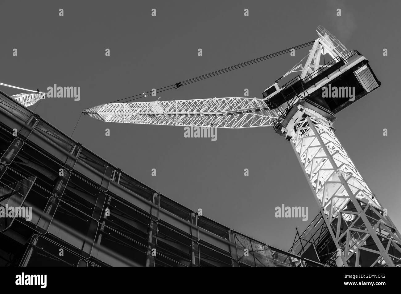 Une grue de construction qui s'élève au-dessus d'un bâtiment et qui brille au soleil. Noir et blanc Banque D'Images