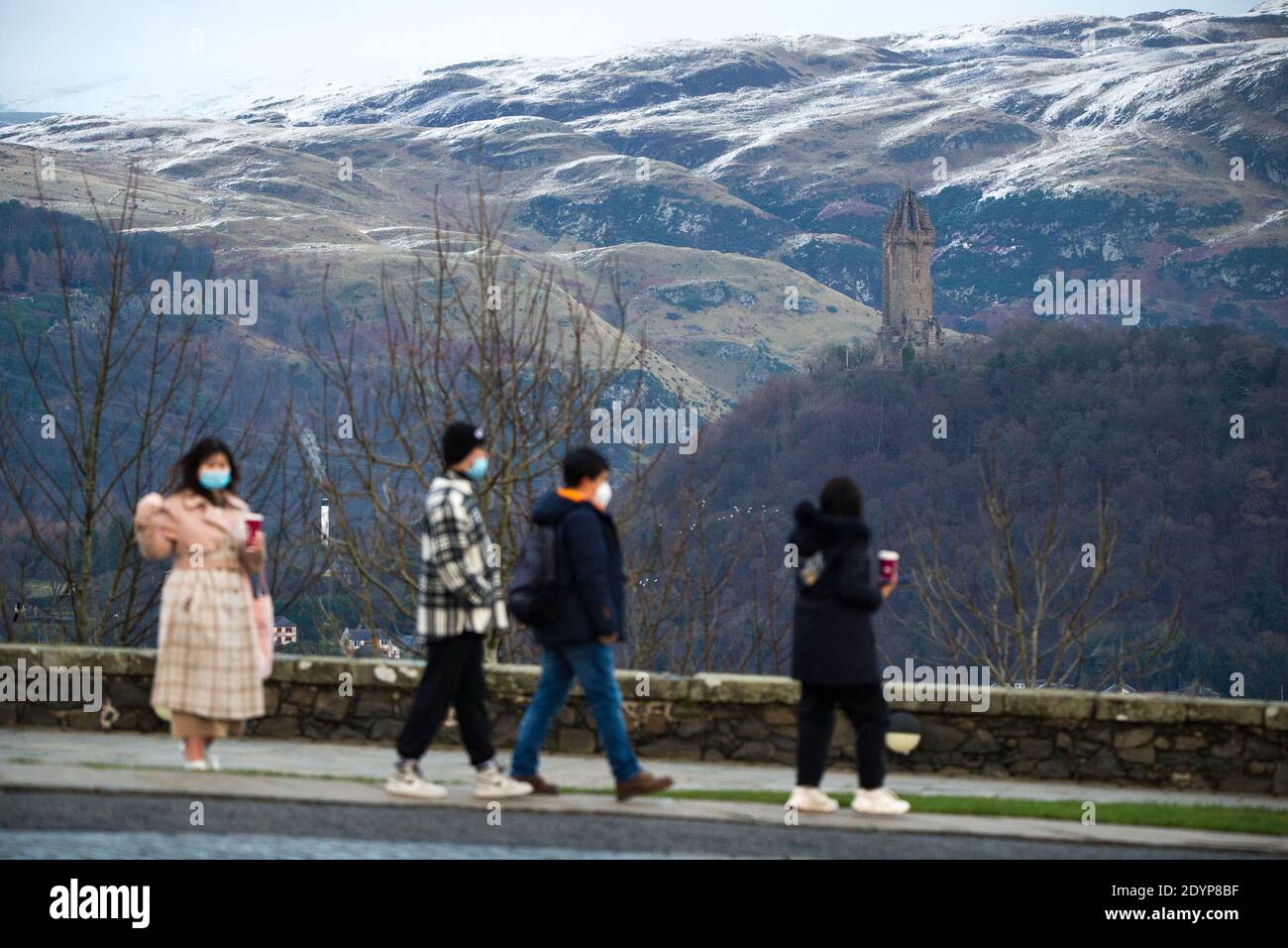 Stirling, Écosse, Royaume-Uni. 27 décembre 2020. Photo : deuxième jour du confinement de la phase 4 festive pour l'Écosse continentale. Un petit groupe de touristes chinois portant des masques de visage regardent sur le Monument Wallace du point de vue du château de Stirling qui offre des vues sur des kilomètres autour. Une petite fenêtre dans le temps émerge de l'avertissement météorologique jaune qui a été émis comme Storm Bella donne la neige chute la nuit laissant une poussière de blanc sur les collines d'Ochill. Crédit : Colin Fisher/Alay Live News Banque D'Images