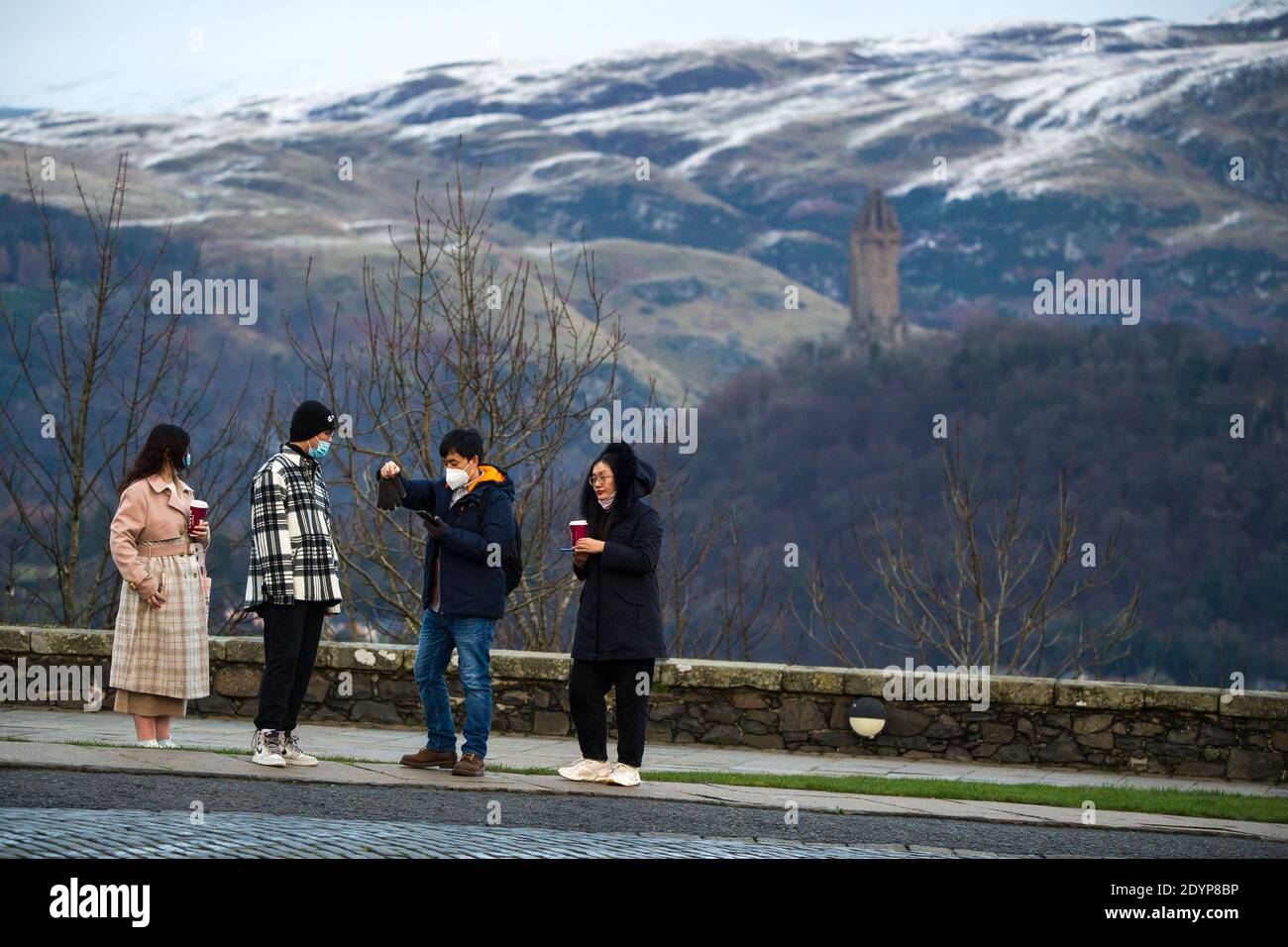Stirling, Écosse, Royaume-Uni. 27 décembre 2020. Photo : deuxième jour du confinement de la phase 4 festive pour l'Écosse continentale. Un petit groupe de touristes chinois portant des masques de visage regardent sur le Monument Wallace du point de vue du château de Stirling qui offre des vues sur des kilomètres autour. Une petite fenêtre dans le temps émerge de l'avertissement météorologique jaune qui a été émis comme Storm Bella donne la neige chute la nuit laissant une poussière de blanc sur les collines d'Ochill. Crédit : Colin Fisher/Alay Live News Banque D'Images