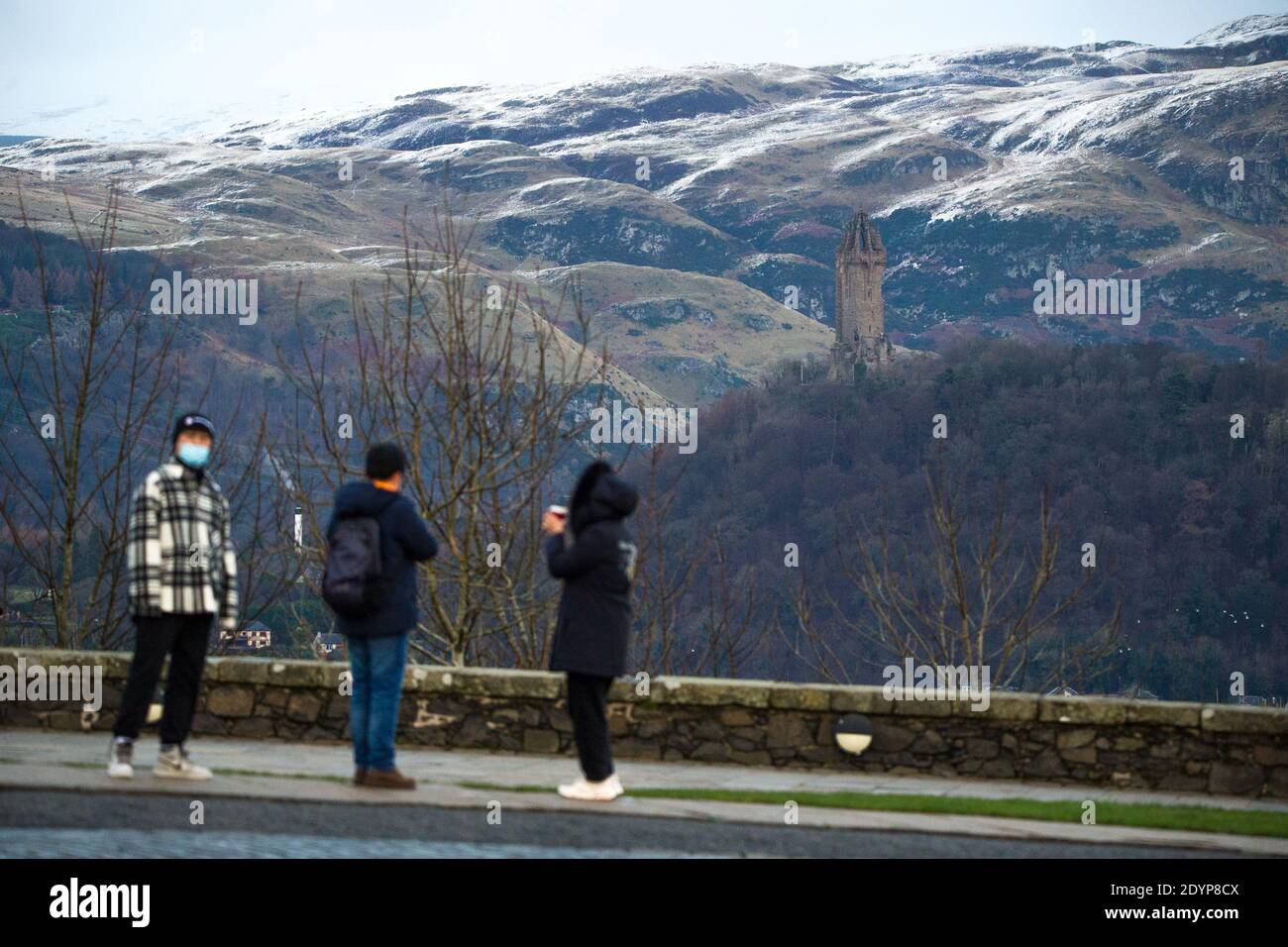 Stirling, Écosse, Royaume-Uni. 27 décembre 2020. Photo : deuxième jour du confinement de la phase 4 festive pour l'Écosse continentale. Un petit groupe de touristes chinois portant des masques de visage regardent sur le Monument Wallace du point de vue du château de Stirling qui offre des vues sur des kilomètres autour. Une petite fenêtre dans le temps émerge de l'avertissement météorologique jaune qui a été émis comme Storm Bella donne la neige chute la nuit laissant une poussière de blanc sur les collines d'Ochill. Crédit : Colin Fisher/Alay Live News Banque D'Images