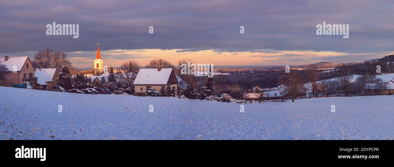 Paysage d'hiver avec champ neigeux et village, lumière du soir illuminant l'église, avion de Vezovata, république Tchèque Banque D'Images