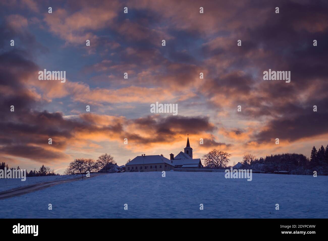 Village avec une église sur une colline au coucher du soleil en hiver, beau ciel avec des nuages illuminés, Vezovata plane, République Tchèque Banque D'Images